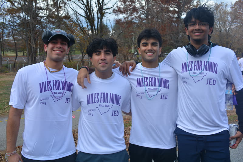 Four friends in matching white Miles for Minds Fall 2025 JED shirts, standing arm in arm outdoors among autumn trees.